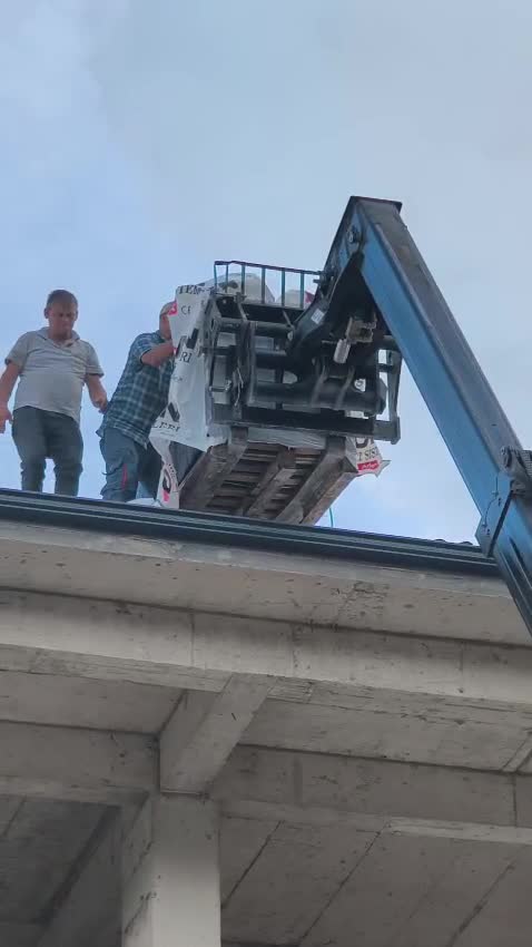 Manitou çalışma platformu çatı döşemesi hizasında, iki işçi malzemeyi kenardan alıyor
