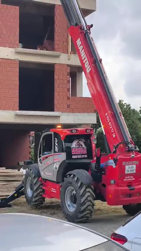 Tuğla kaba inşaata dik açıyla yük çıkaran kırmızı Manitou MT 1840, tepe lambası yanıyor